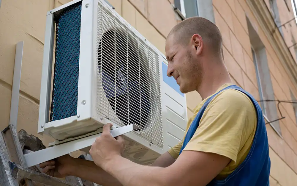 Technician installing an air conditioning unit on building exterior