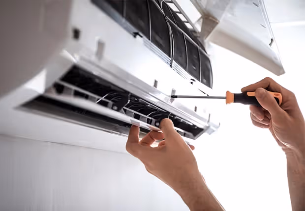 Technician repairing air conditioning unit with screwdriver