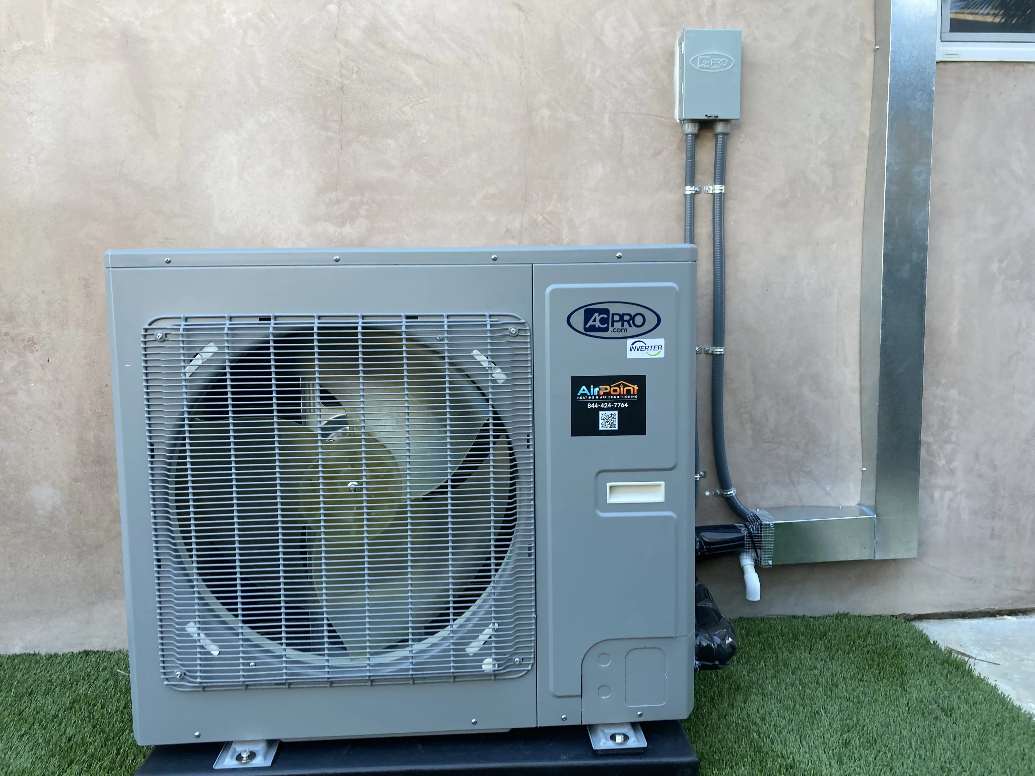 AC Pro inverter heat pump unit installed on exterior wall with grass