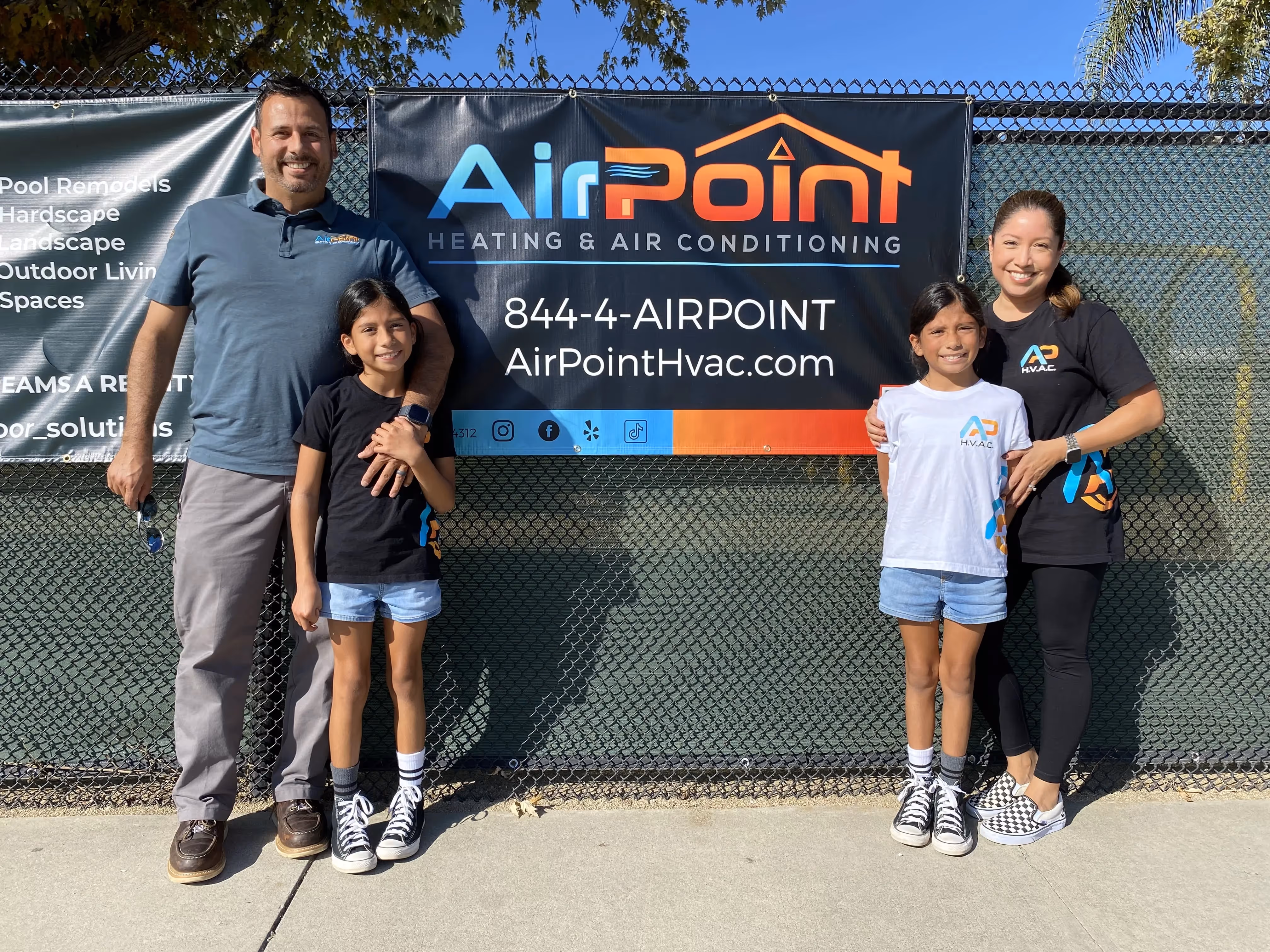 Family of four posing in front of AirPoint Heating & Air Conditioning banner