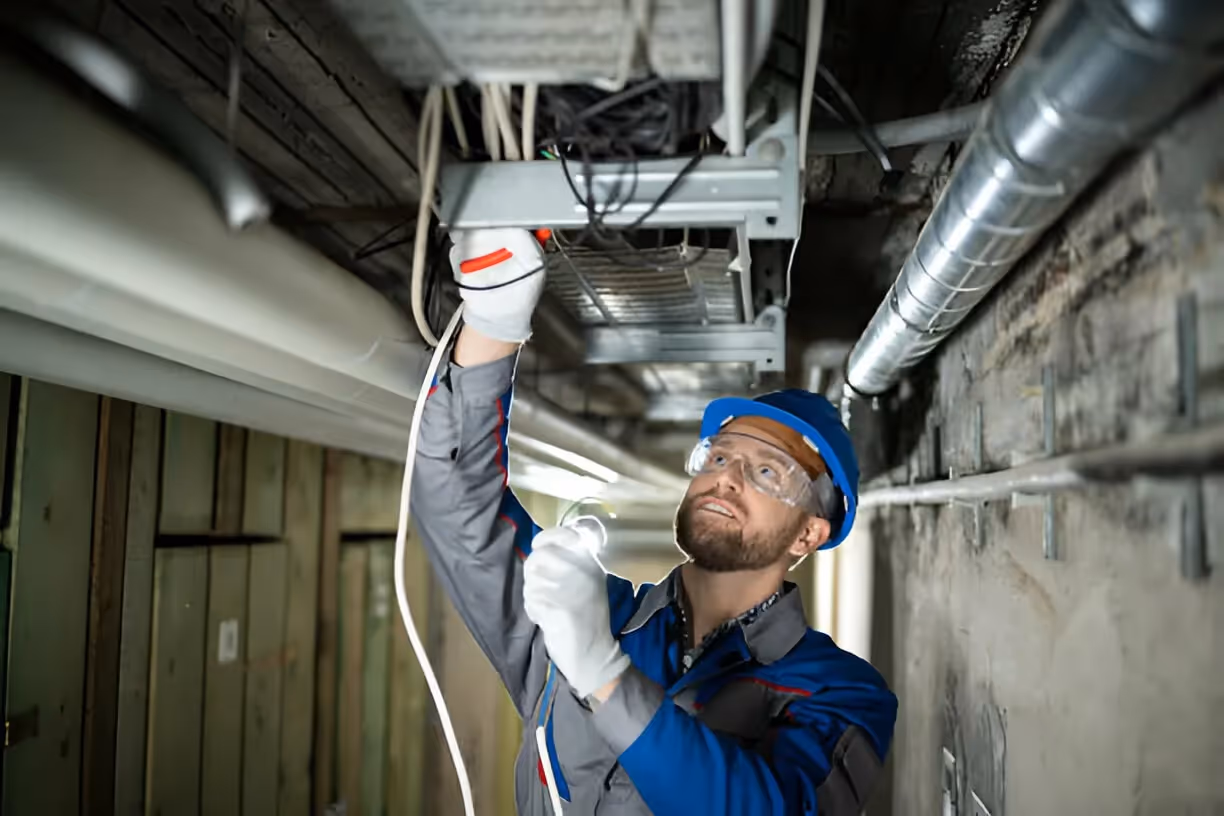 Technician in safety gear installing electrical wiring in ceiling infrastructure