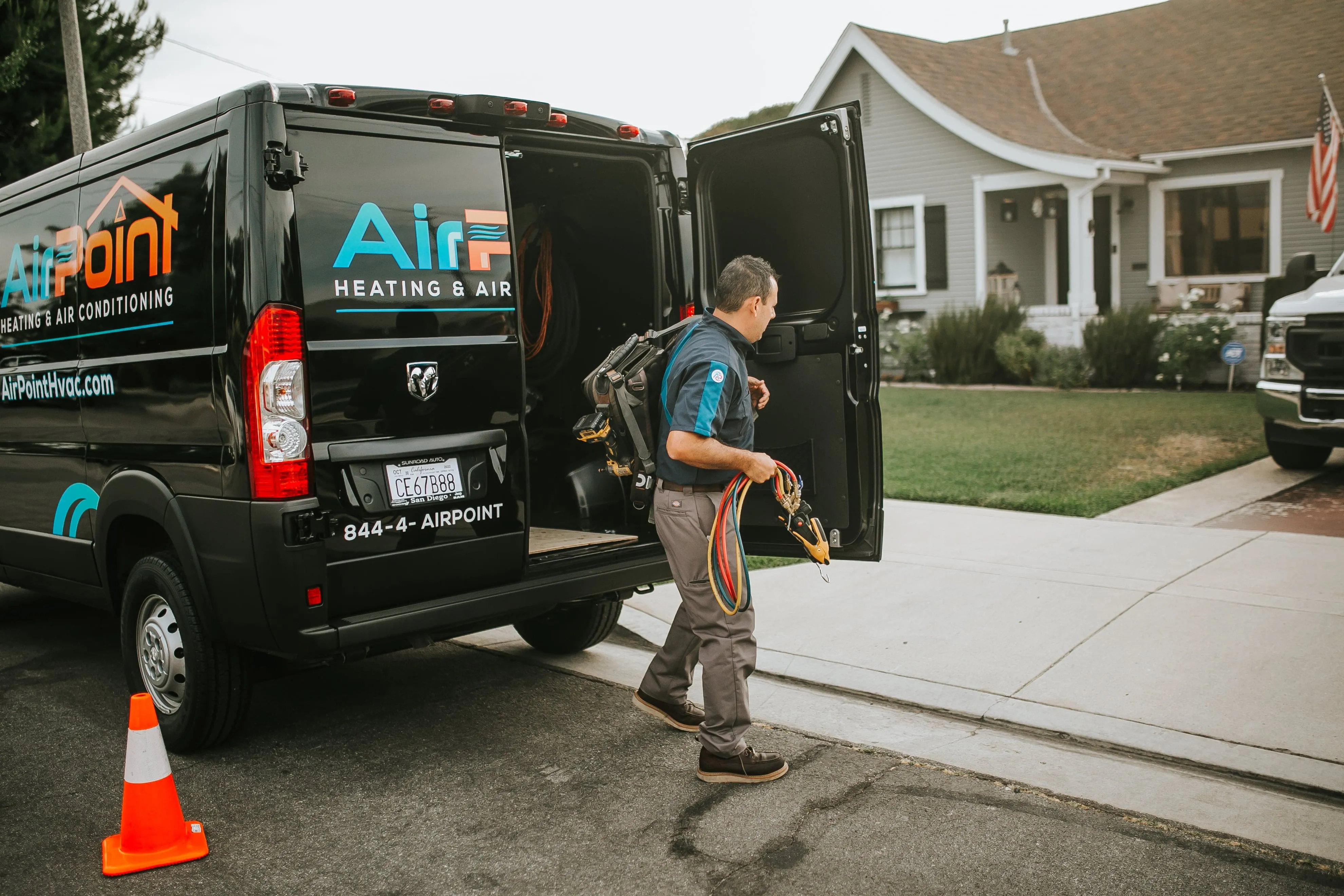 AirPoint HVAC technician carrying equipment near service van in residential area