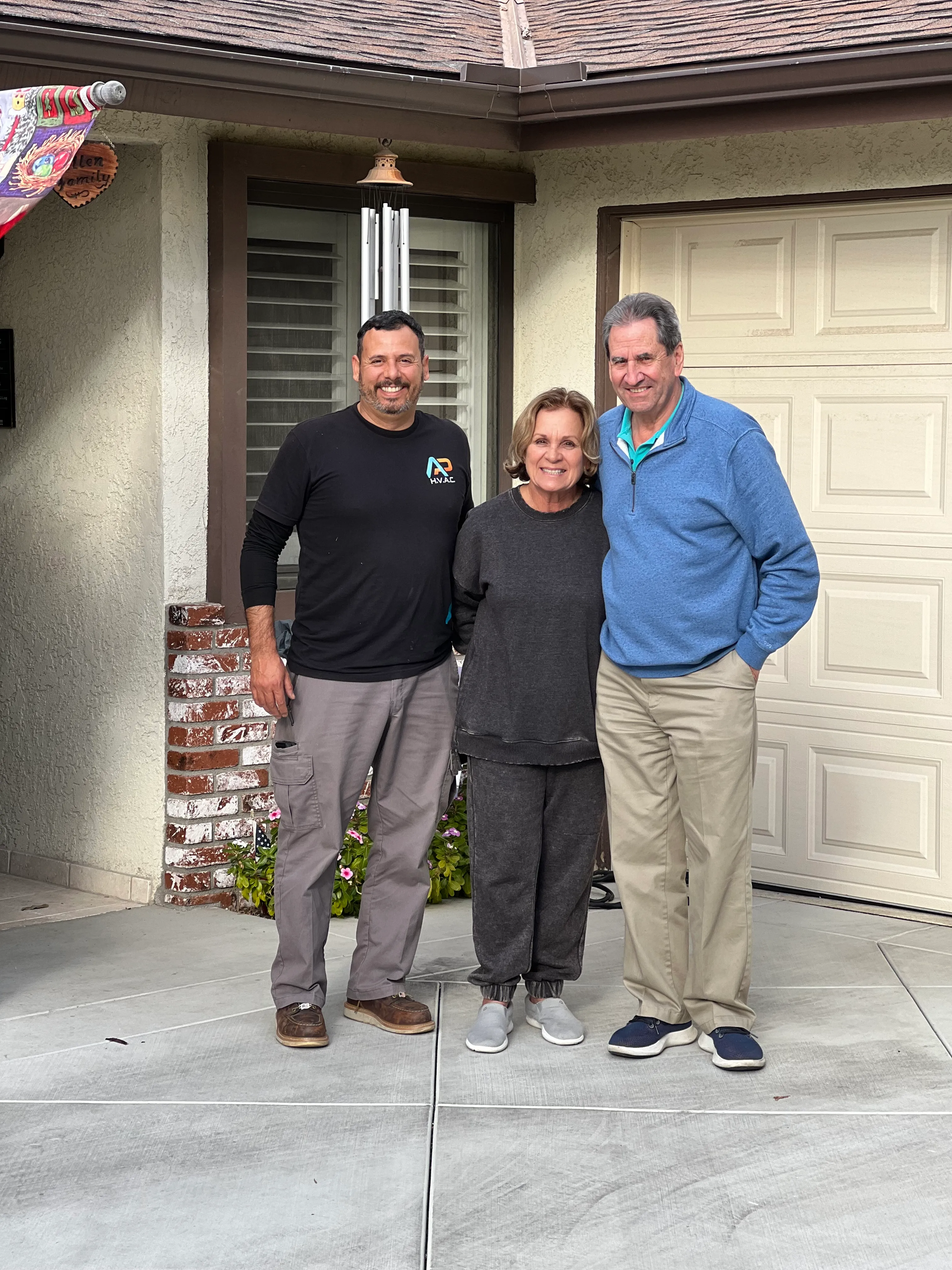 Three people smiling together outside a house with a garage door