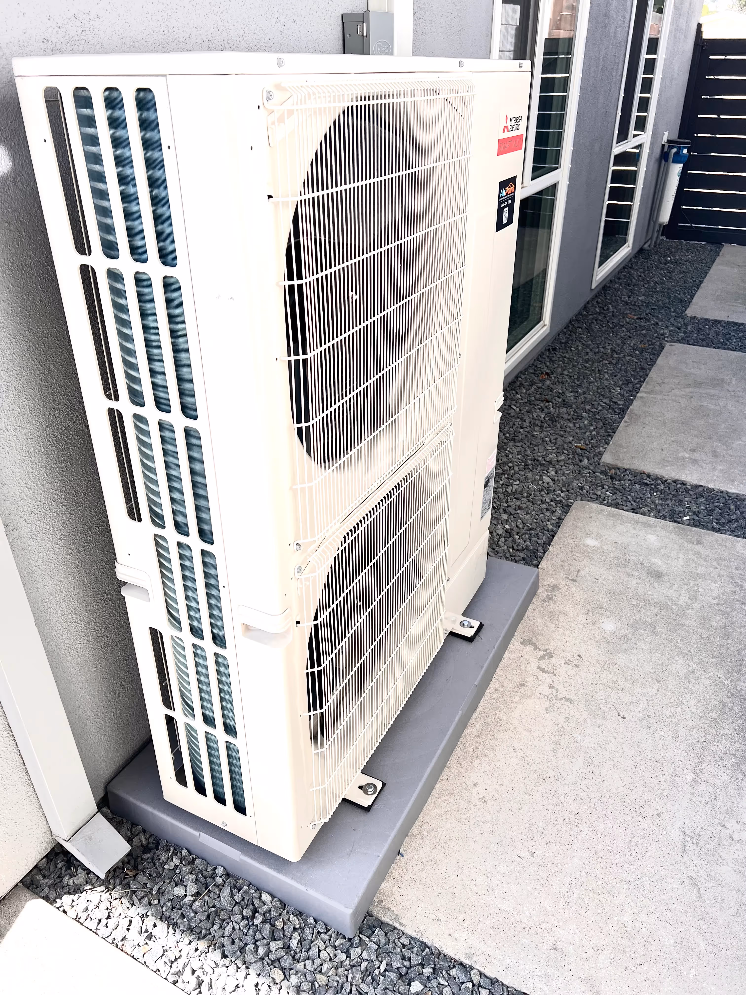 Large white air conditioning unit mounted outside on concrete and gravel