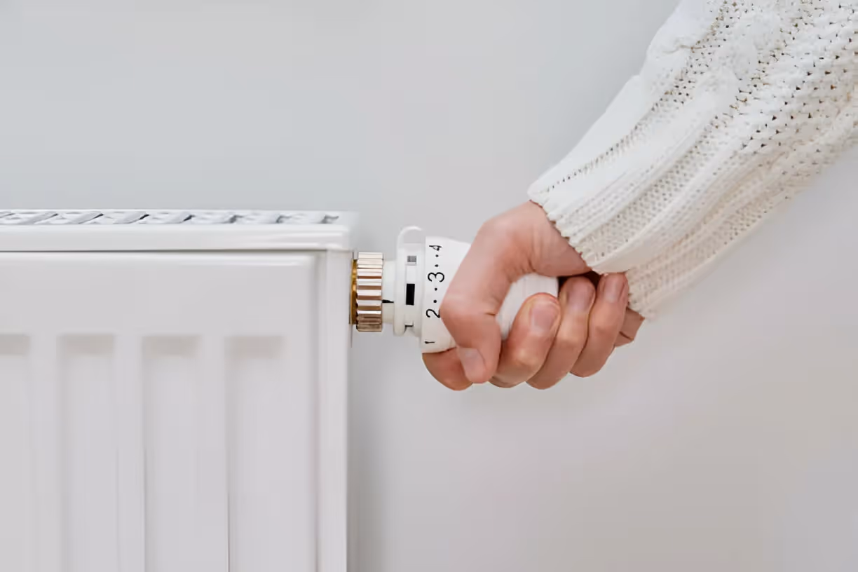 Hand adjusting thermostat on a white radiator heating system