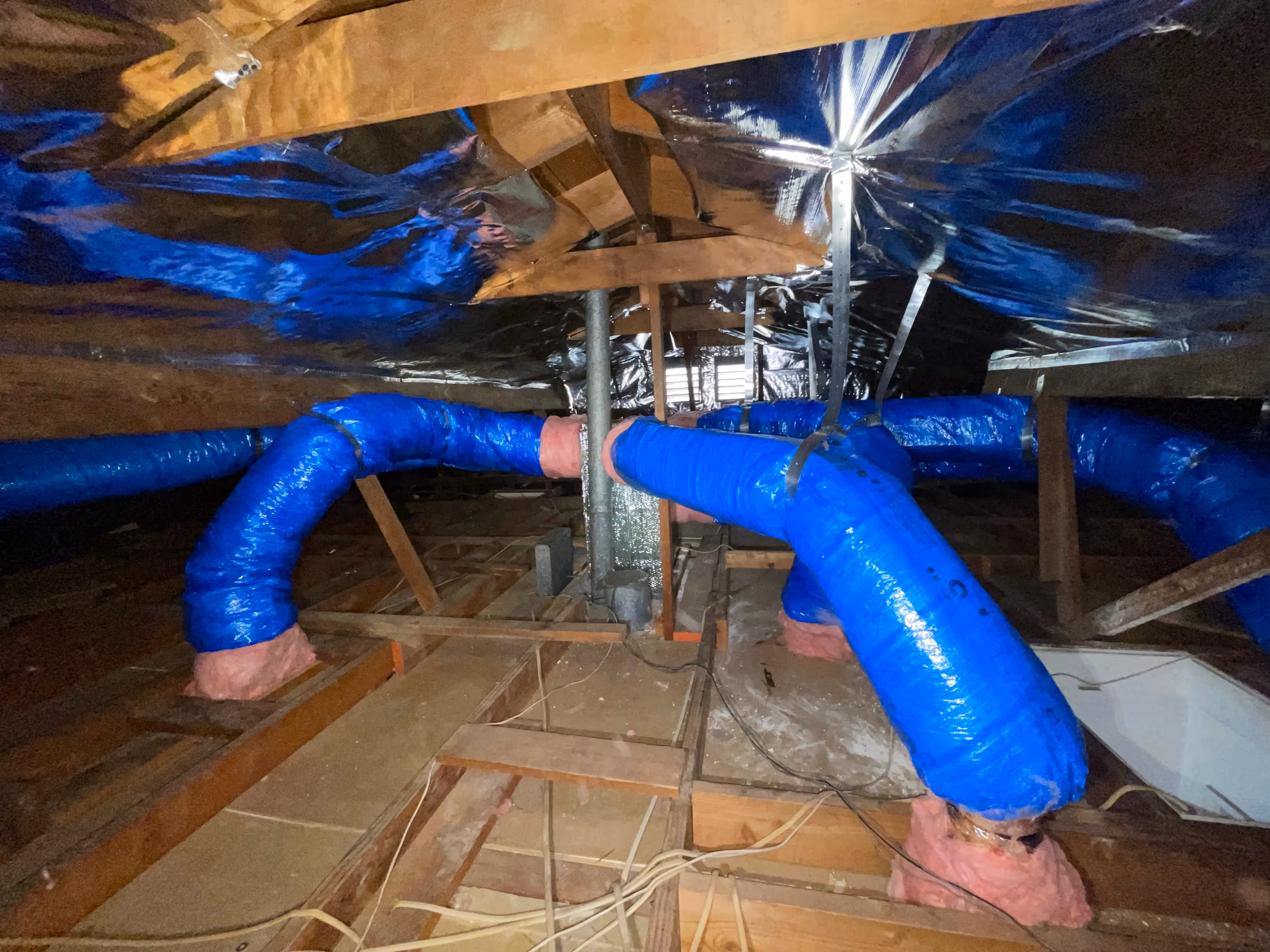 Blue insulated ducts in wooden attic crawl space with metal support
