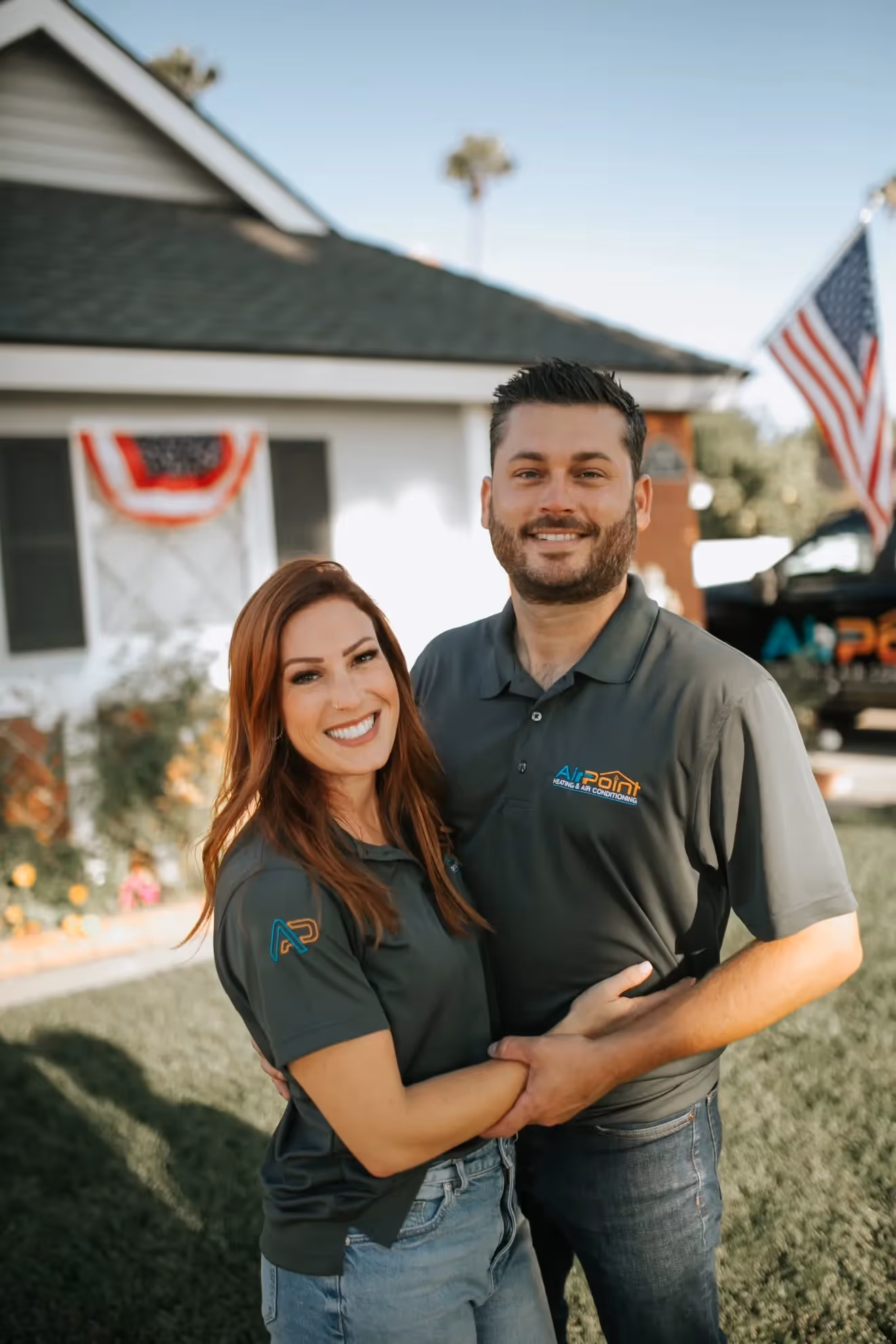 Smiling couple in matching Air Point shirts standing in front of house