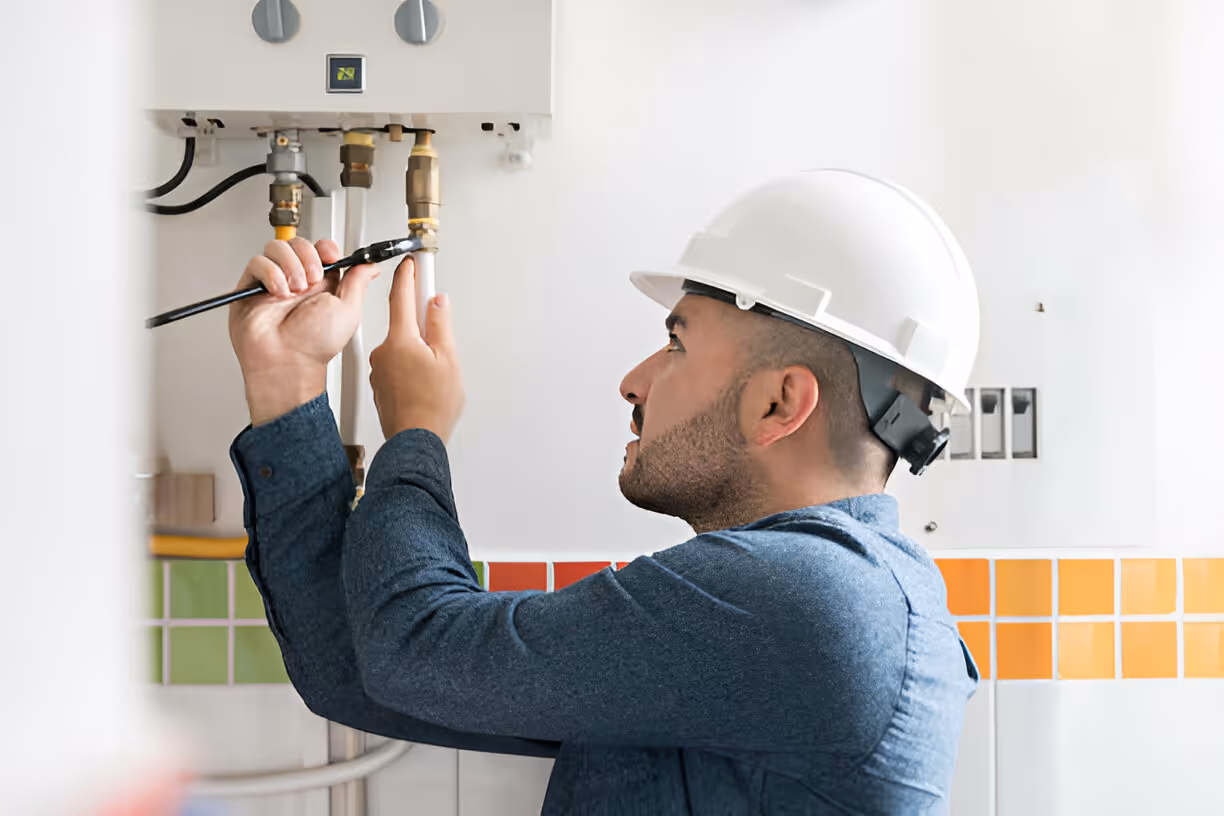Technician in hard hat fixing pipes near colorful tiled wall