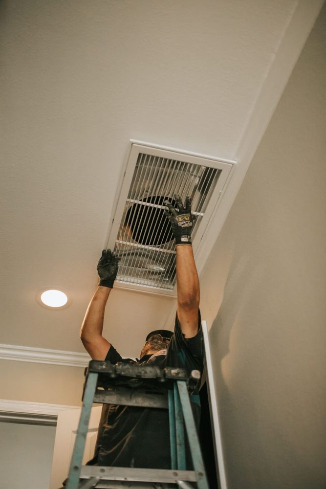 HVAC technician on ladder removing or installing an air vent grille on a ceiling during AC maintenance