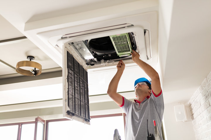 Technician repairing ceiling-mounted air conditioning unit indoors