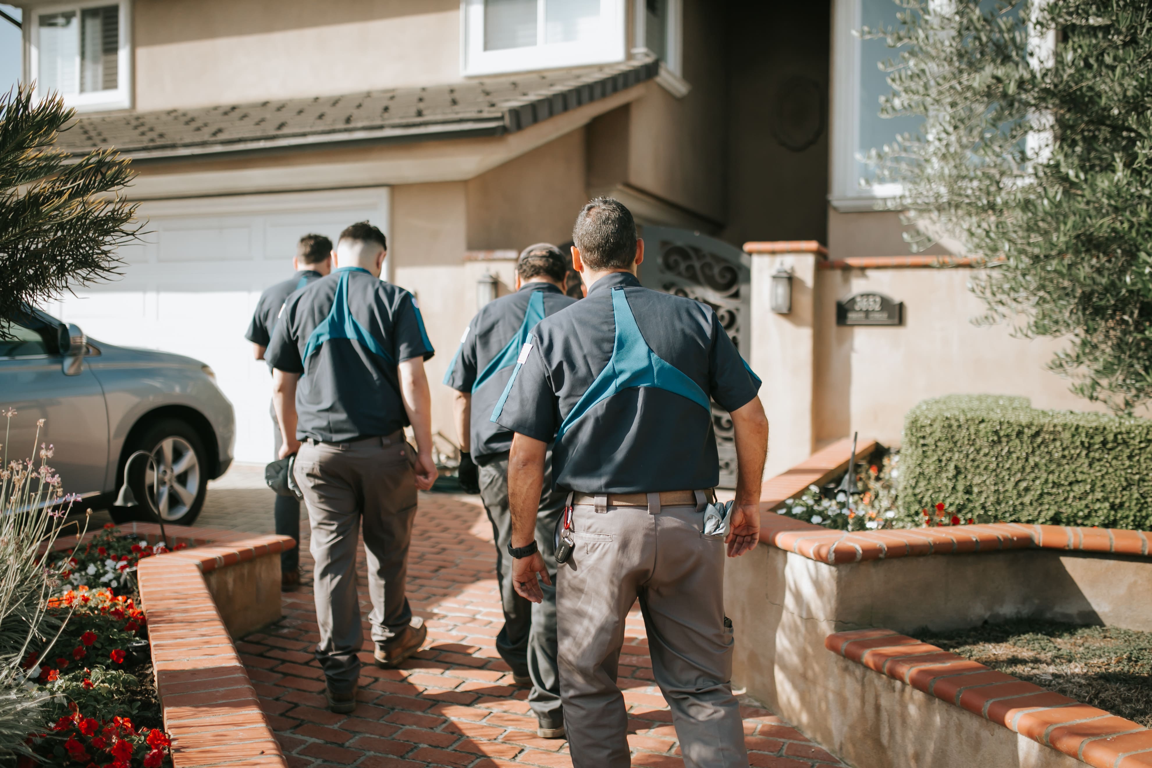 Workers in blue and gray uniforms walking along brick pathway near house