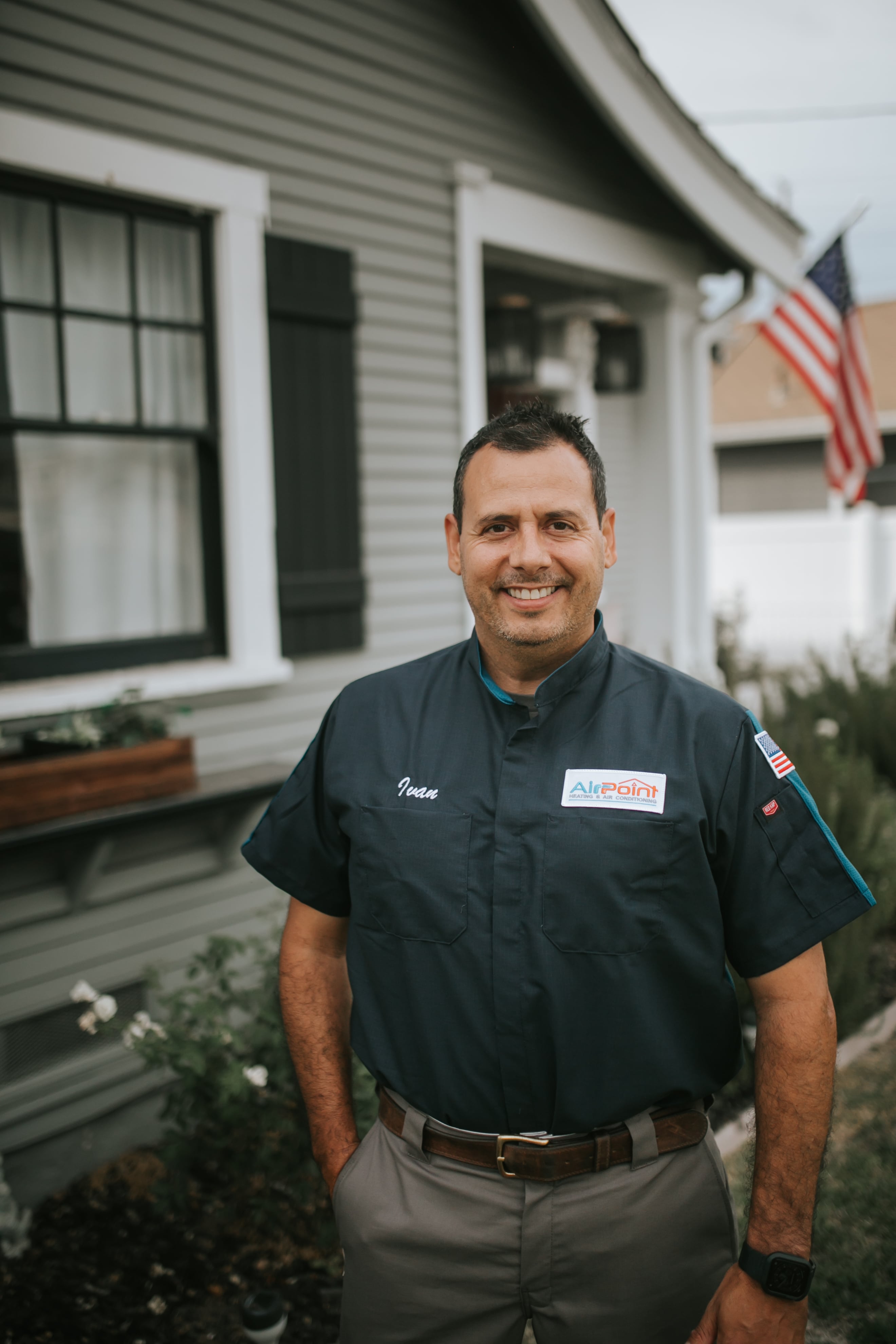 Smiling technician in uniform standing in front of house with American flag