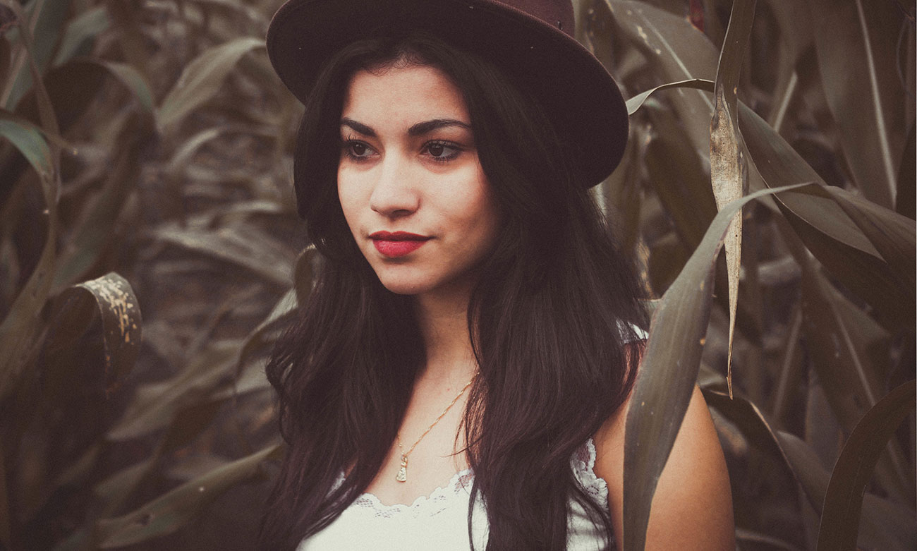 Woman in black hat standing among leaves with thoughtful expression