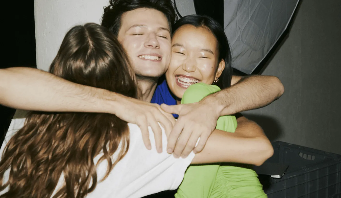 Three people are smiling and embracing each other in a group hug.
