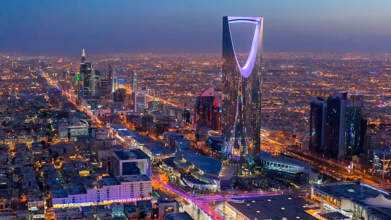 Nighttime aerial view of Riyadh city showcasing the illuminated Kingdom Centre Tower and surrounding skyscrapers with city lights.