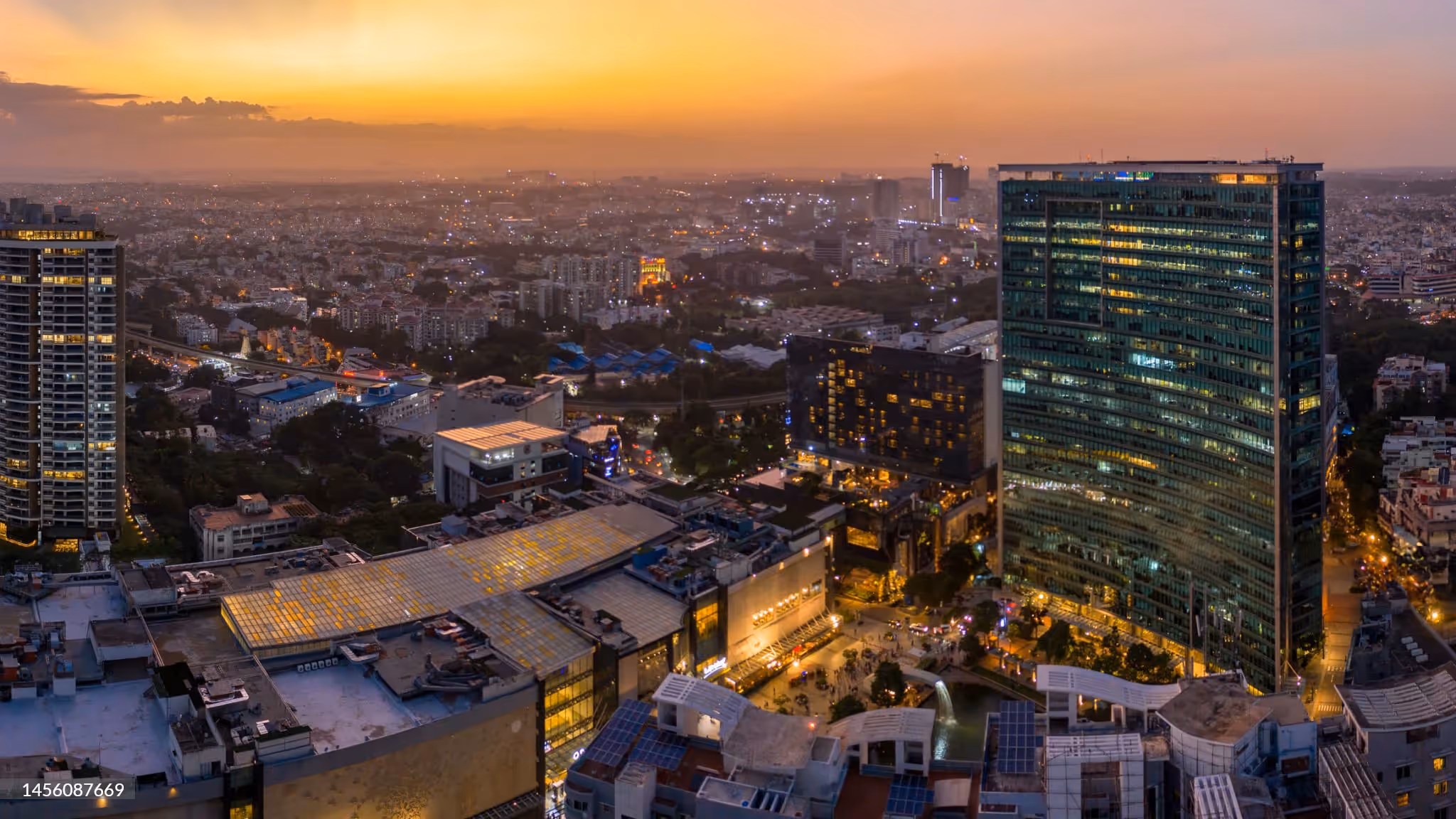 Aerial view of a cityscape at sunset with high-rise buildings and illuminated streets.