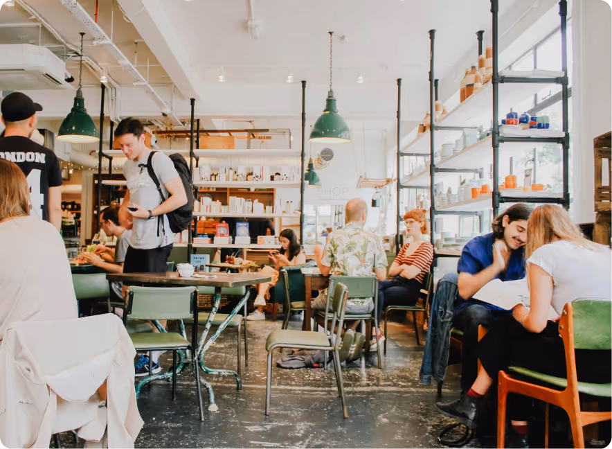 Bright café interior with people sitting and chatting at tables, surrounded by shelves with pottery and books.