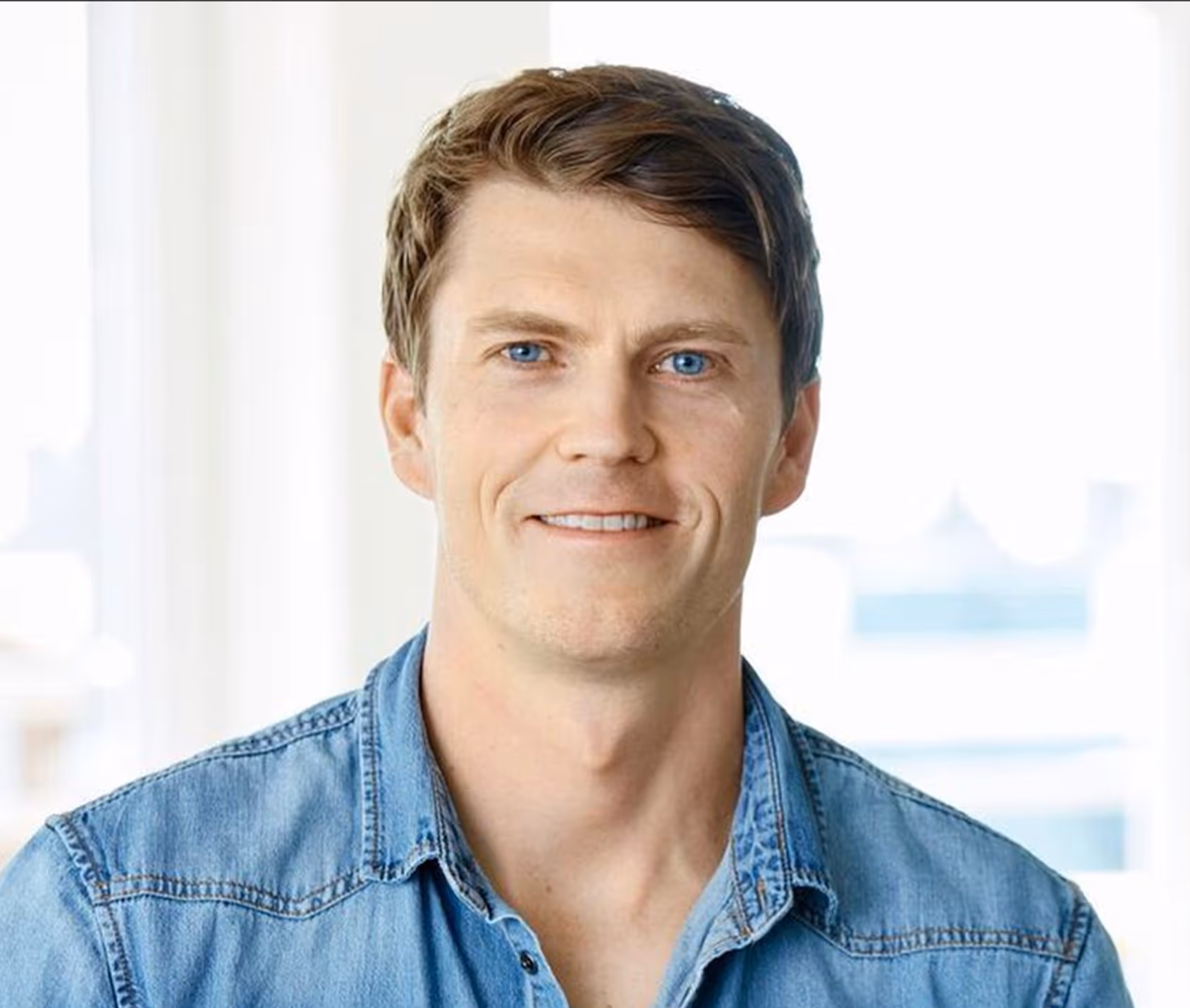 Smiling man with blue eyes and short brown hair wearing a blue denim shirt.
