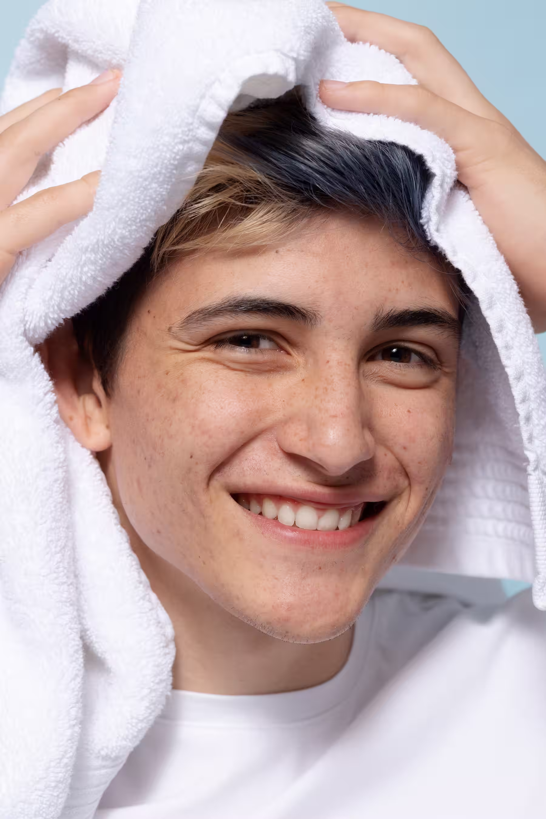 Jeune homme souriant tenant une serviette blanche sur sa tête avec un fond bleu clair.