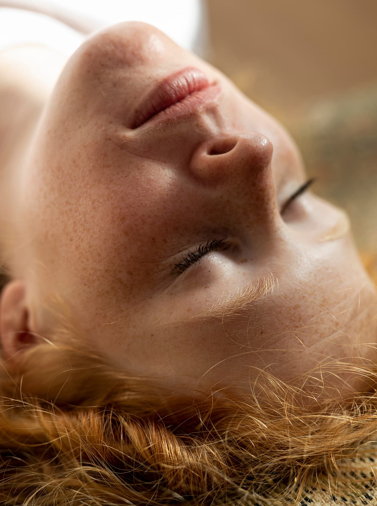 Visage féminin allongé vers le haut avec peau claire, taches de rousseur et cheveux roux.