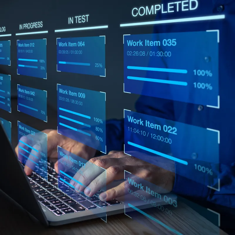 Person typing on a laptop keyboard with overlaid digital project management dashboard showing work items in progress, in test, and completed statuses with progress bars and timestamps.