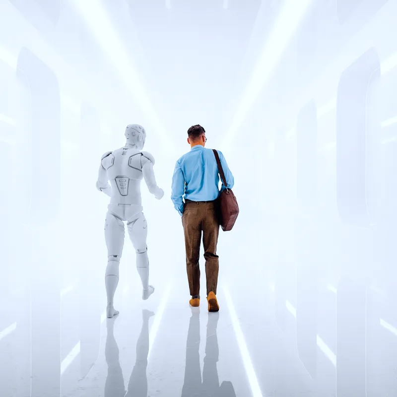 A man in business attire walking down a futuristic white hallway alongside a humanoid robot.