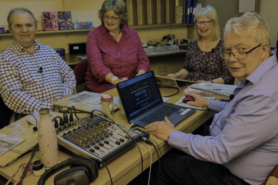 Four people round a table with recording equipment ready to record the news.