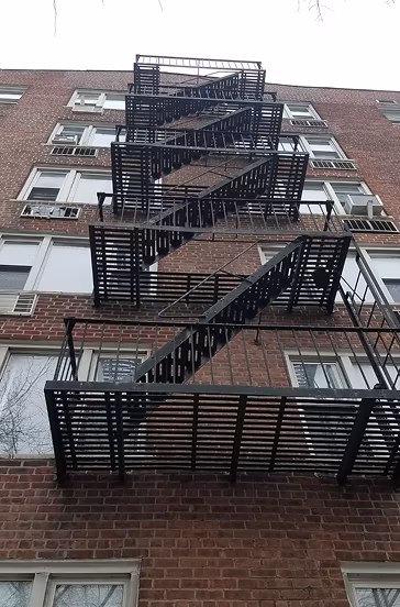 Black metal fire escape stairs zigzagging down the exterior of a red brick apartment building.