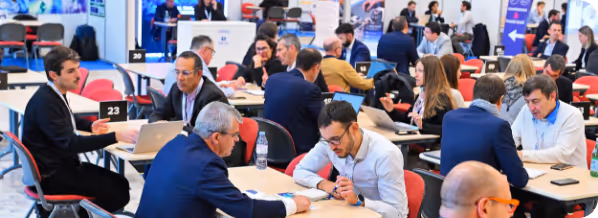 Professionals in business attire having discussions and working on laptops at a networking event.
