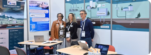 Trois professionnels debout devant un stand d'exposition avec des affiches et des ordinateurs portables.