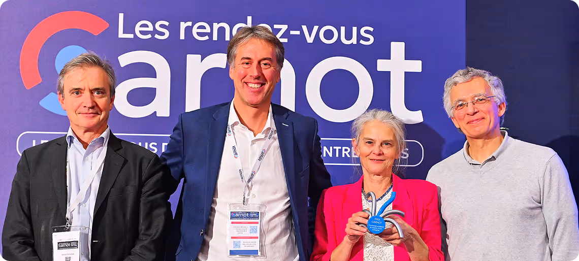 Quatre personnes souriantes posant devant un panneau Carnot, une tient un trophée bleu