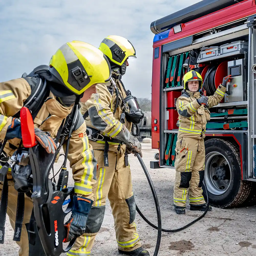 Brandweerlieden bereiden een inzet met het Coolfire-systeem voor. Eén collega activeert het bedieningspaneel op het blusvoertuig, terwijl anderen de lans en slang klaarmaken. De foto illustreert de samenwerking en praktische toepasbaarheid van het systeem tijdens trainingen en cursussen.