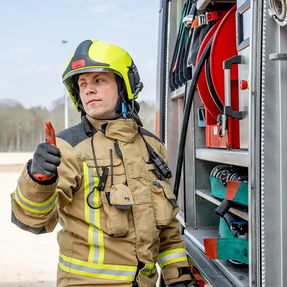 Brandweerman geeft een duim omhoog naast een blusvoertuig met Coolfire-uitrusting. Het moment symboliseert vertrouwen en gereedheid na afronding van de Coolfire-gebruikerstraining: klaar voor veilige en effectieve inzet.