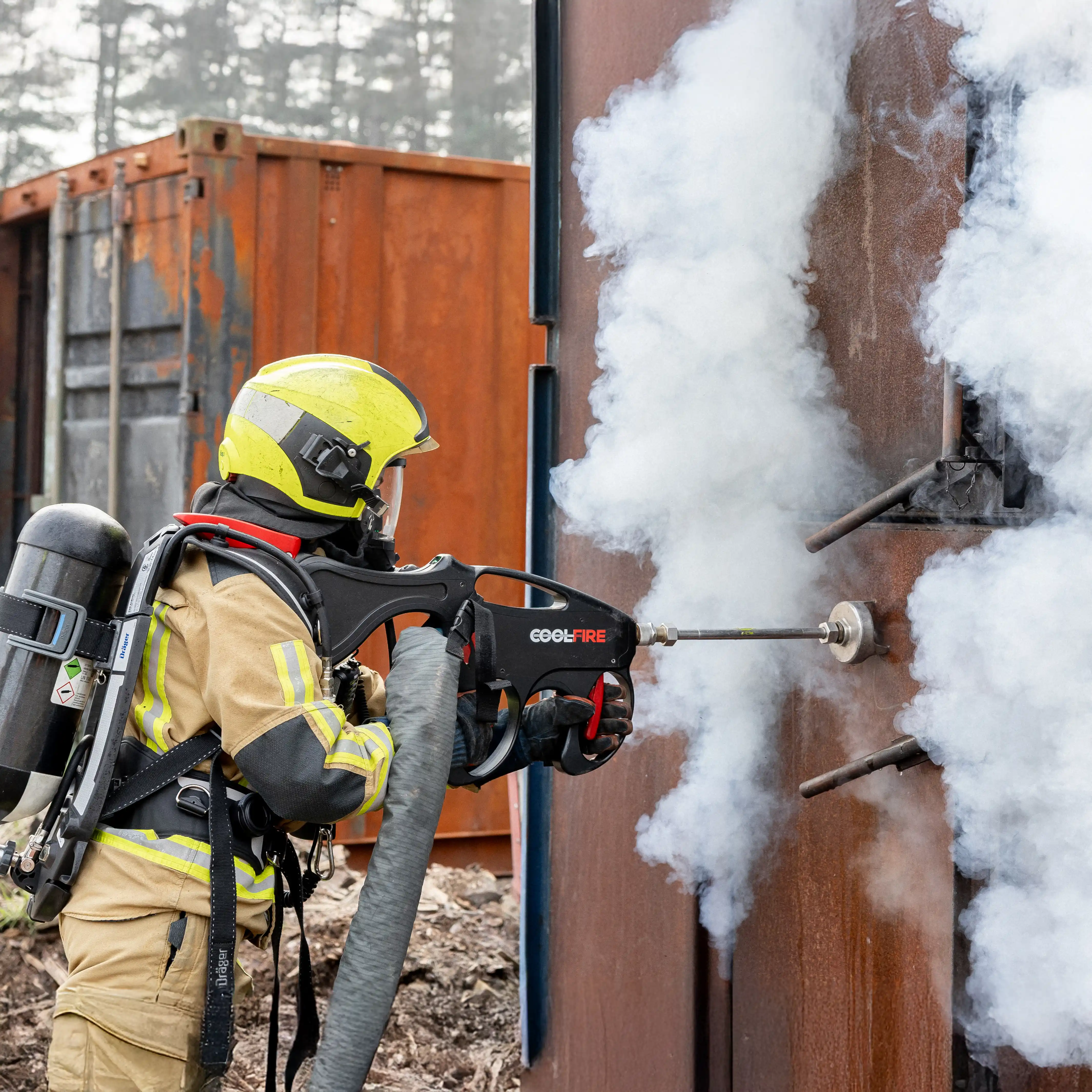 Brandweerman voert fase 2 van de Coolfire-methode uit: het vernevelen van water door een metalen wand om rookgassen snel te koelen. De fijne nevel zorgt voor effectieve inertisatie van het compartiment, zonder binnentreden.