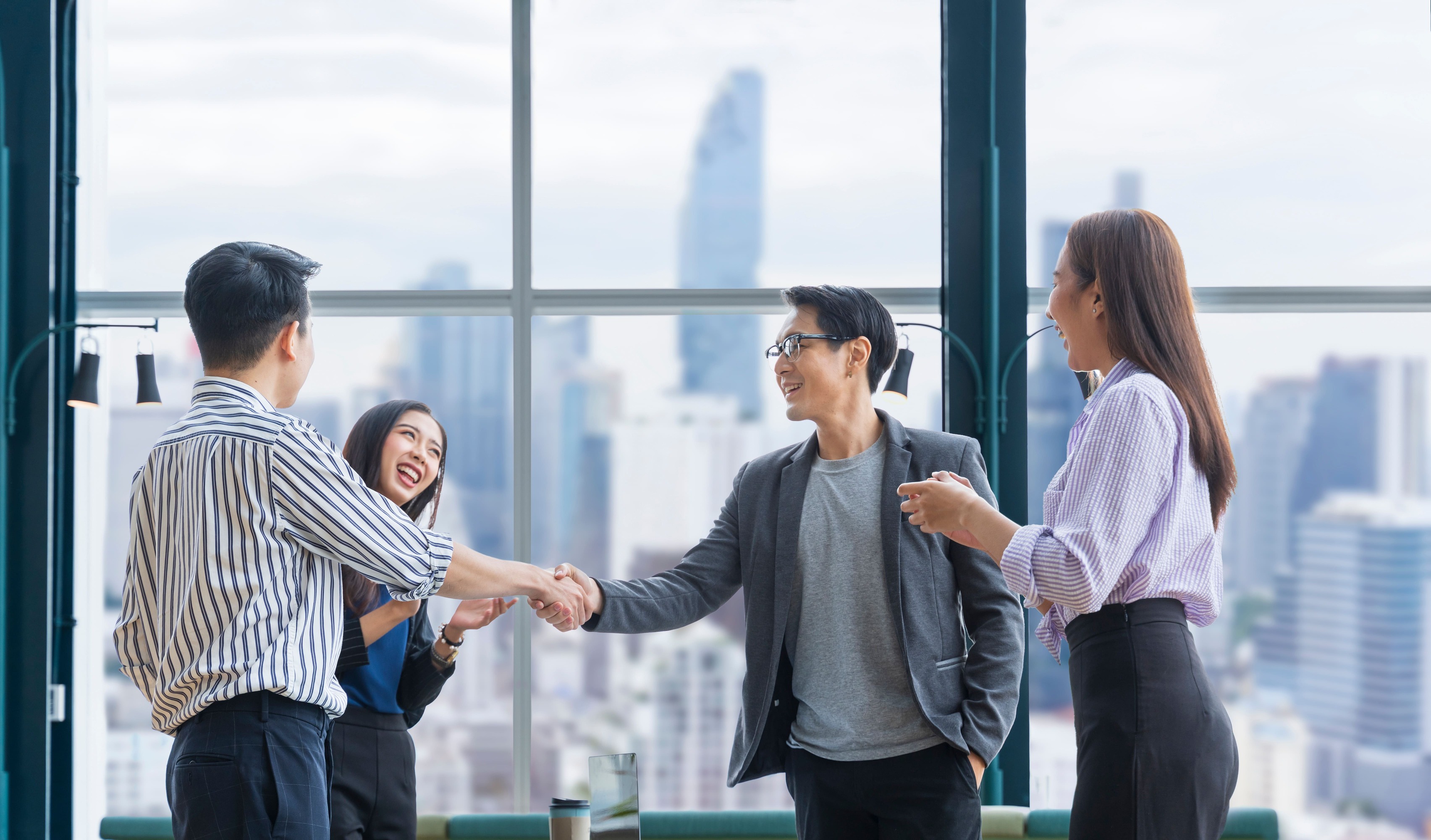 A group of business people shaking hands in a modern office with a skyline view.