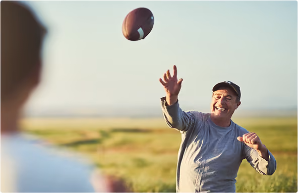 Two men throw a football to each other outdoors during a sunny day
