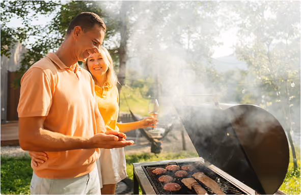 A man and woman outside on a sunny day talking while cooking on a grill