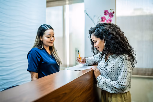 A woman with curly hair signs papers during check in at the front desk of a wellness clinic