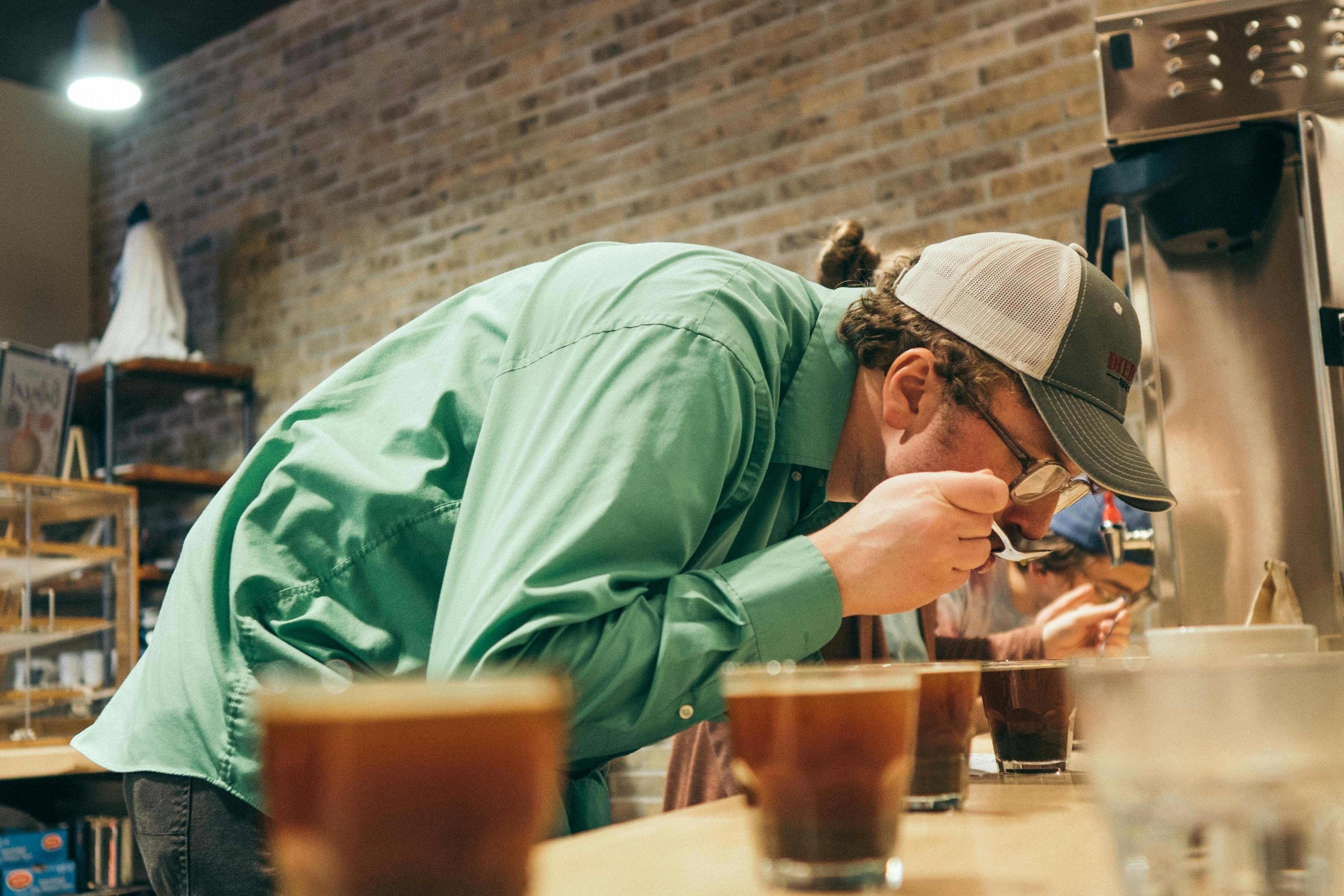 a man in a green shirt and hat leaning over a table with drinks