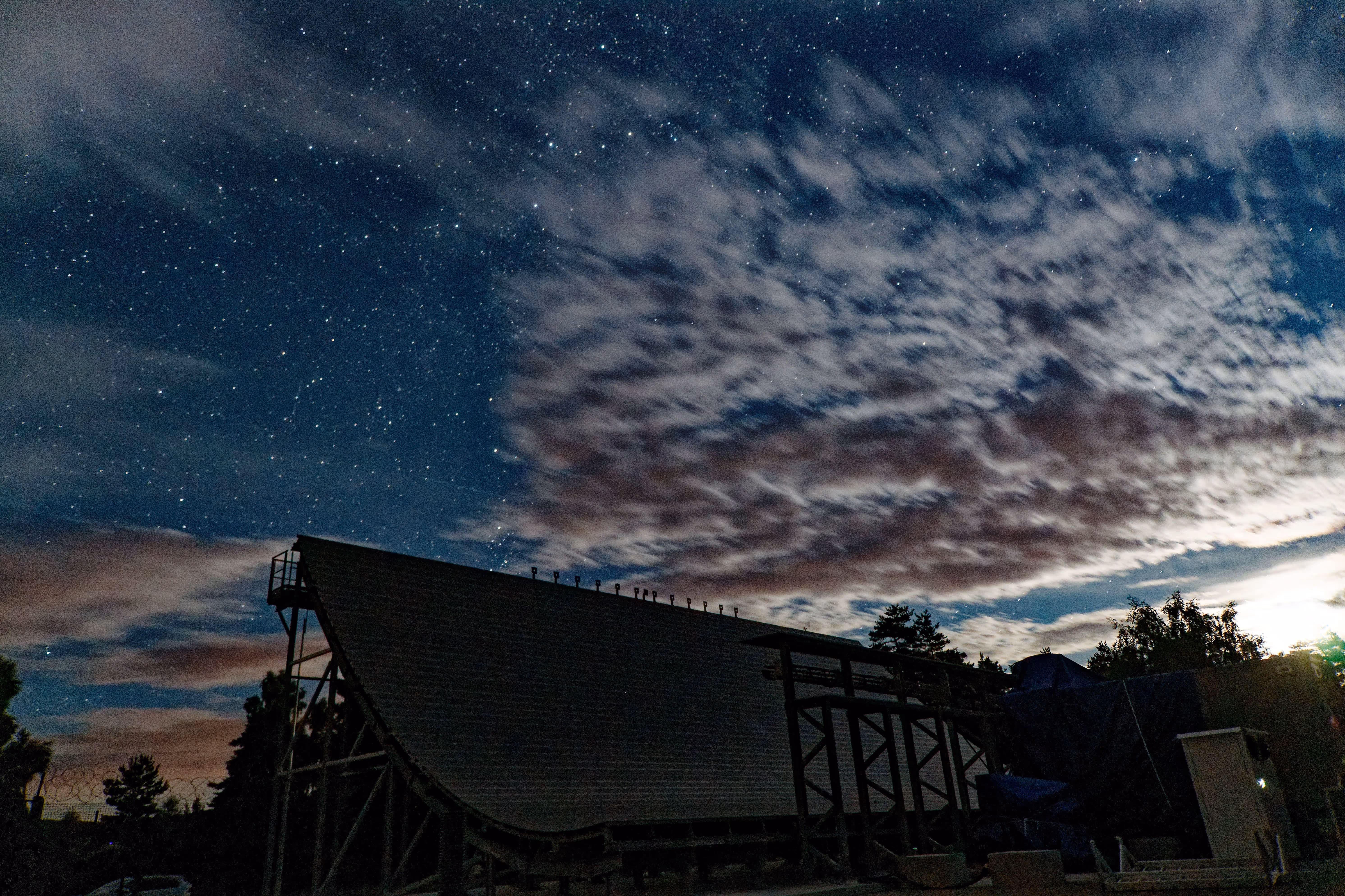 Large wooden half-pipe ramp silhouetted under a starry night sky with scattered clouds.