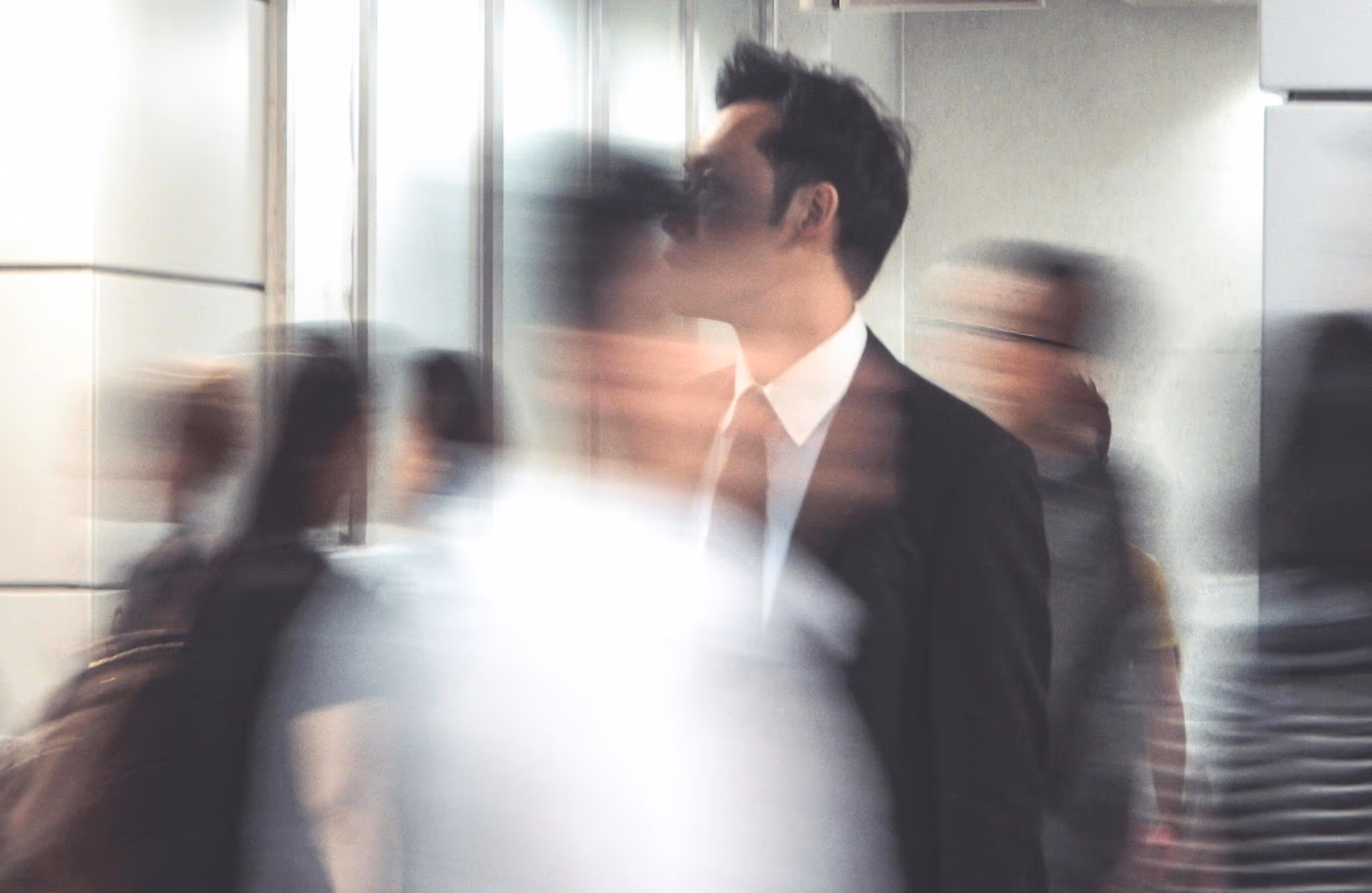 Man in a suit standing still while blurred people move quickly around him in a modern indoor setting.