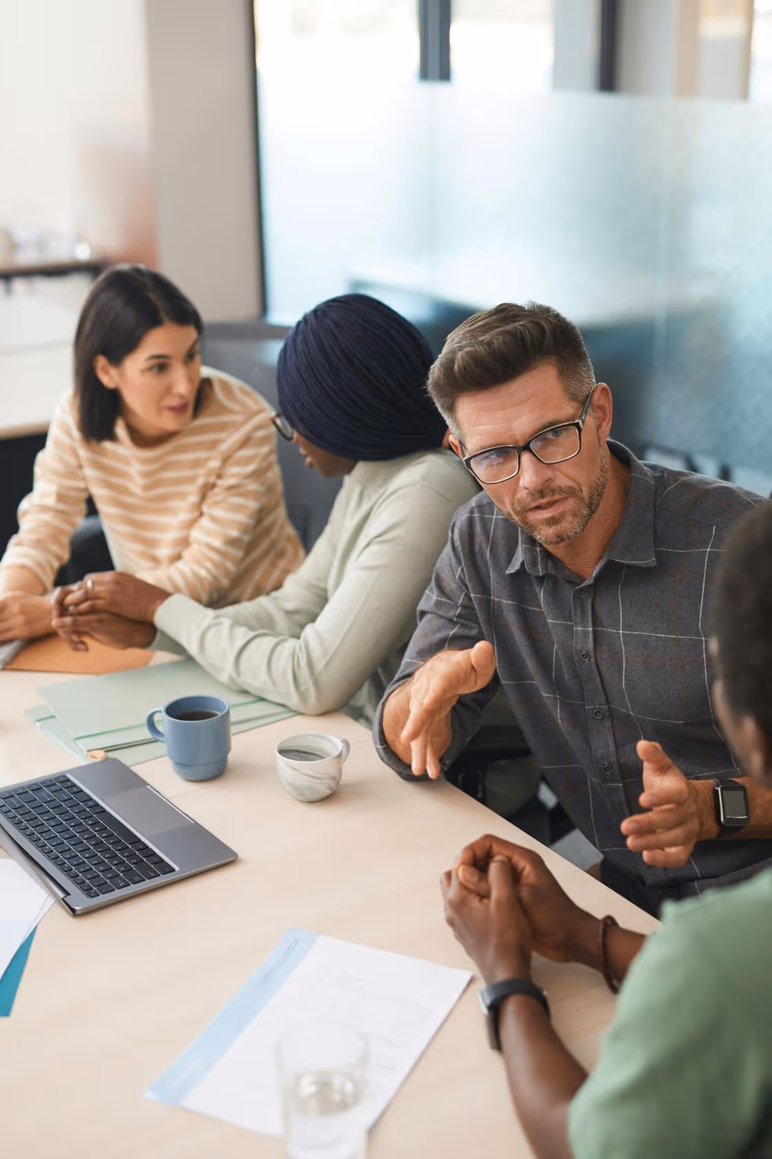 Four diverse colleagues in discussion around a table with laptops and documents in an office.