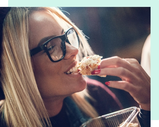 smiling blond woman with glasses taking a bite of food