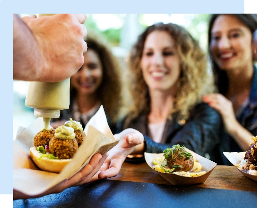 hands finishing making a falafel sandwich and handing it to a customer