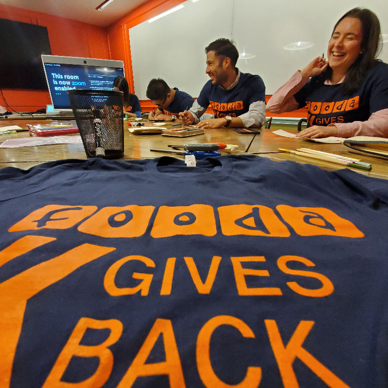 closeup of a Fooda Gives Back t-shirt with people volunteering in the background