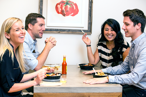 4 coworkers laughing eating together at a table.