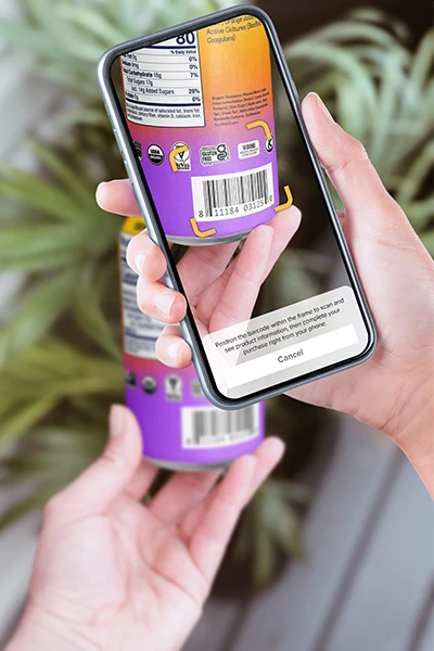 Hands holding a phone and drink can, scanning the barcode using Fooda's scan to pay feature.