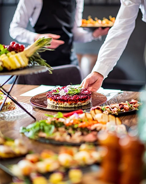 A server placing a plate with a decorative layered dish among a table of colorful catered food.