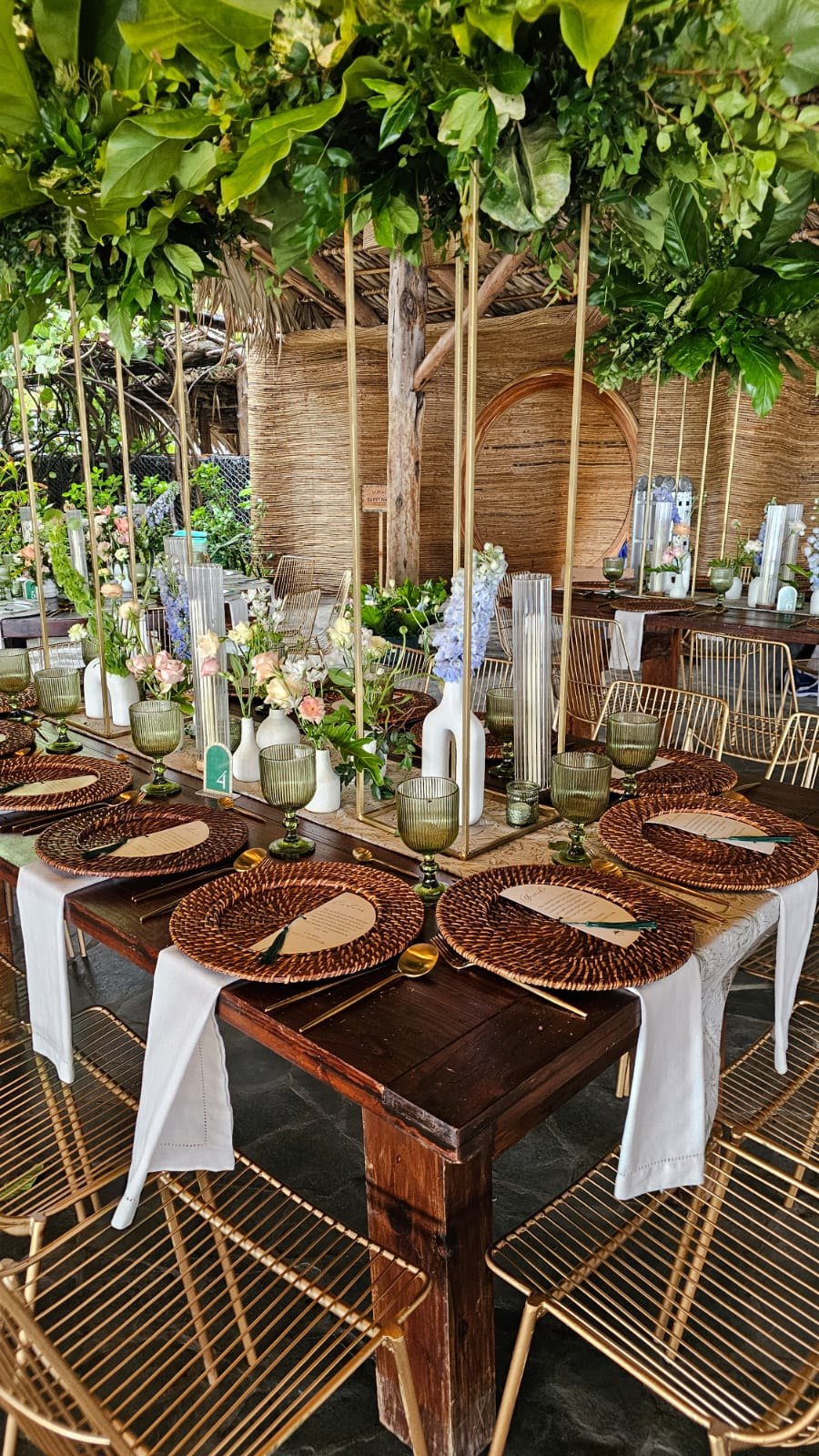 Wedding reception table with tropical flowers, woven chargers and green glassware