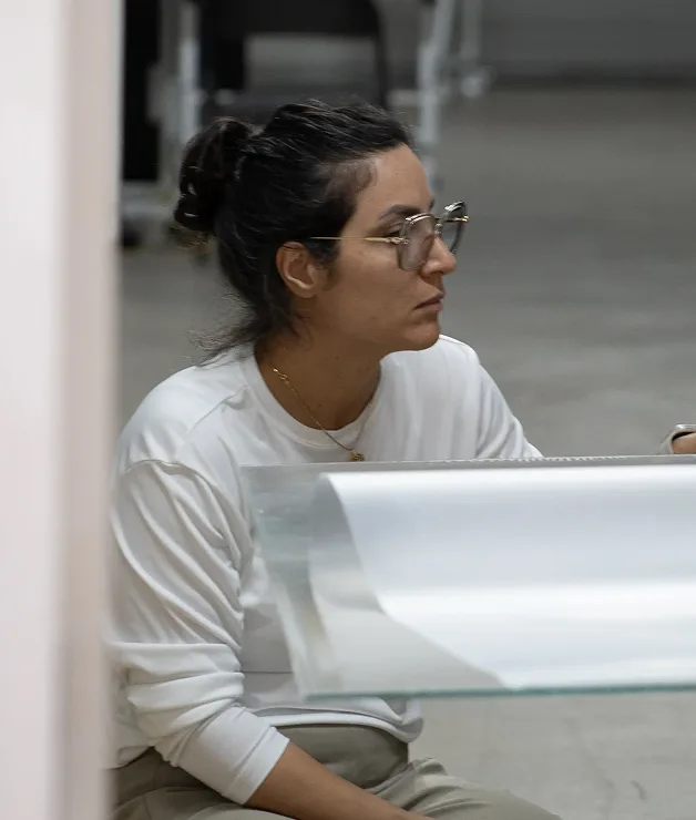 Focused team member in glasses and a white shirt working with clear material inside a workshop or lab space.